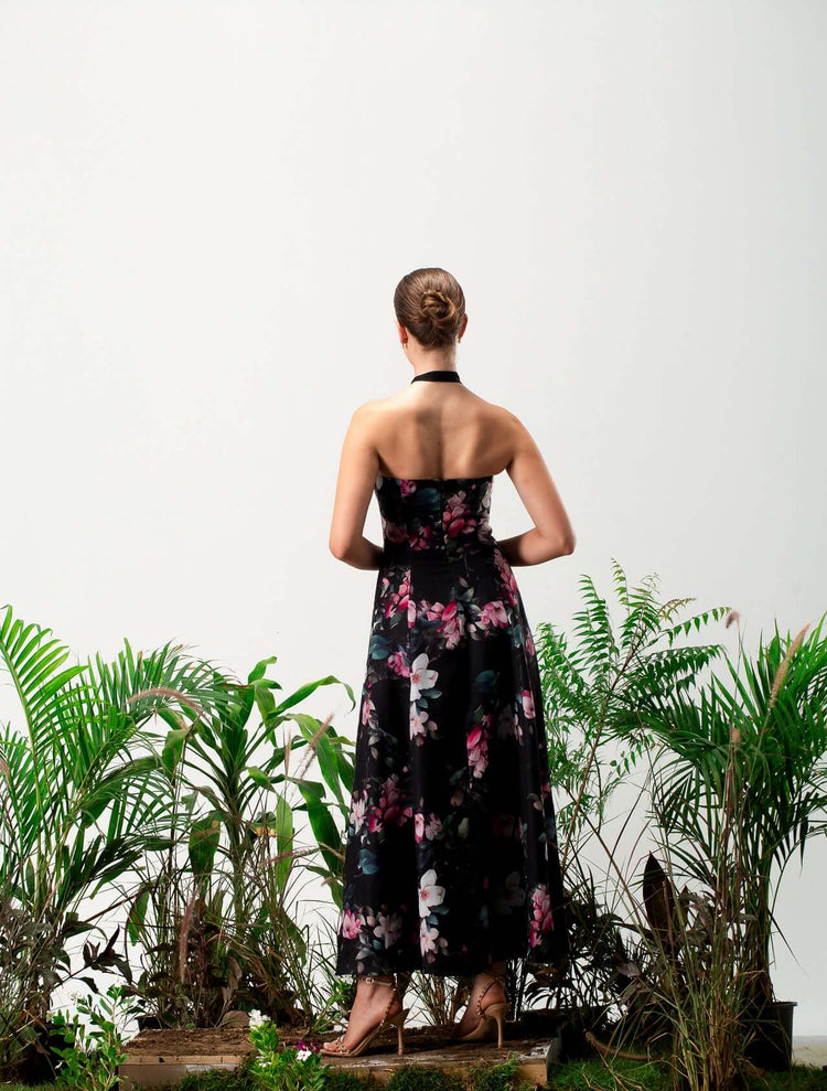 Woman in a halter neck floral maxi dress standing among green plants, back view