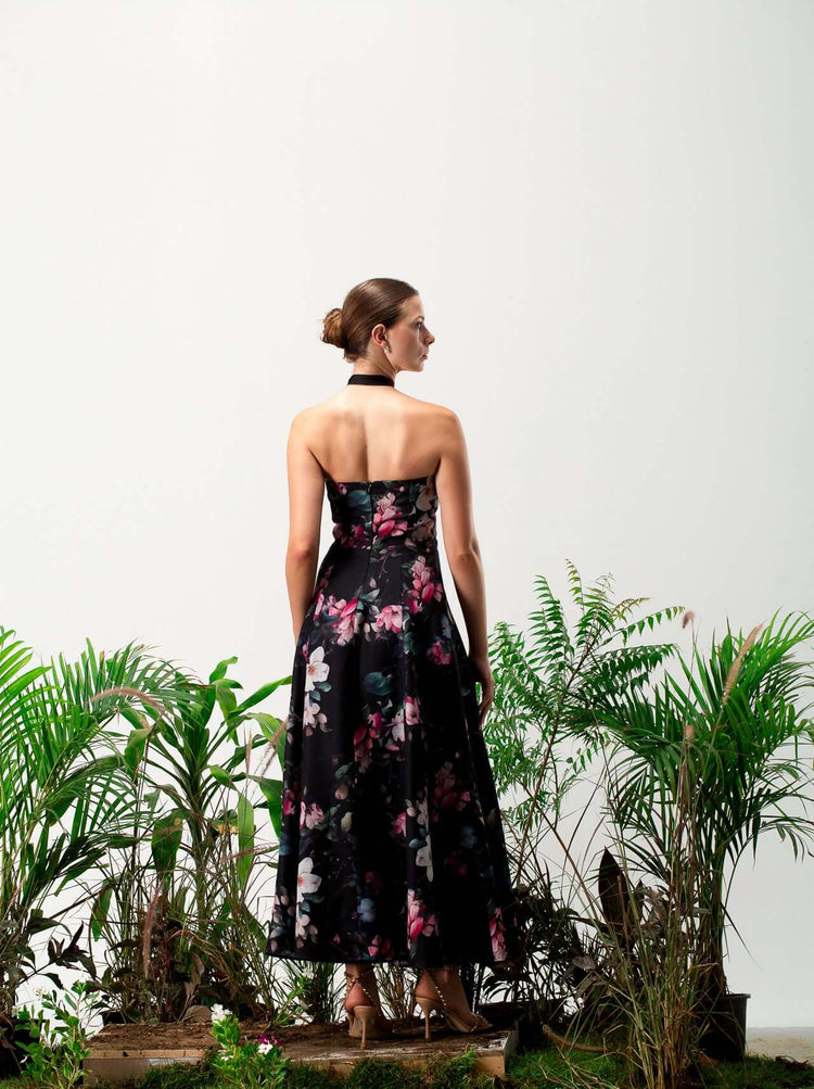 Woman in black floral strapless dress with halter neck, standing among green plants