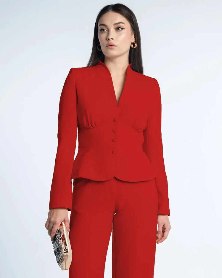 Woman wearing a tailored red suit with fitted blazer and pants, holding embellished clutch.