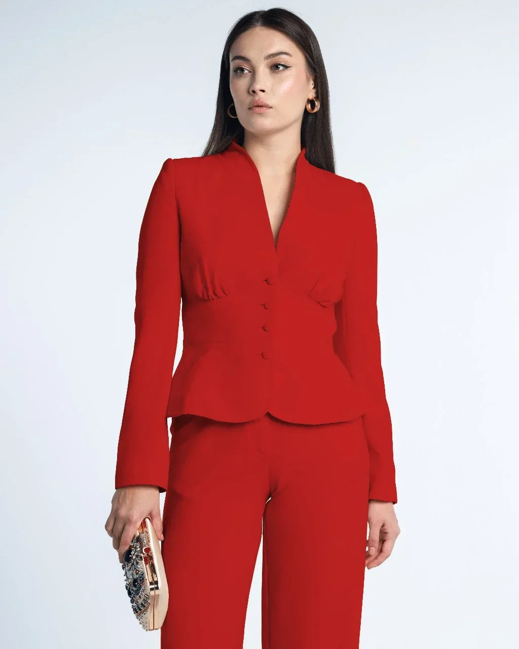 Woman wearing a tailored red suit with fitted blazer and pants, holding embellished clutch.