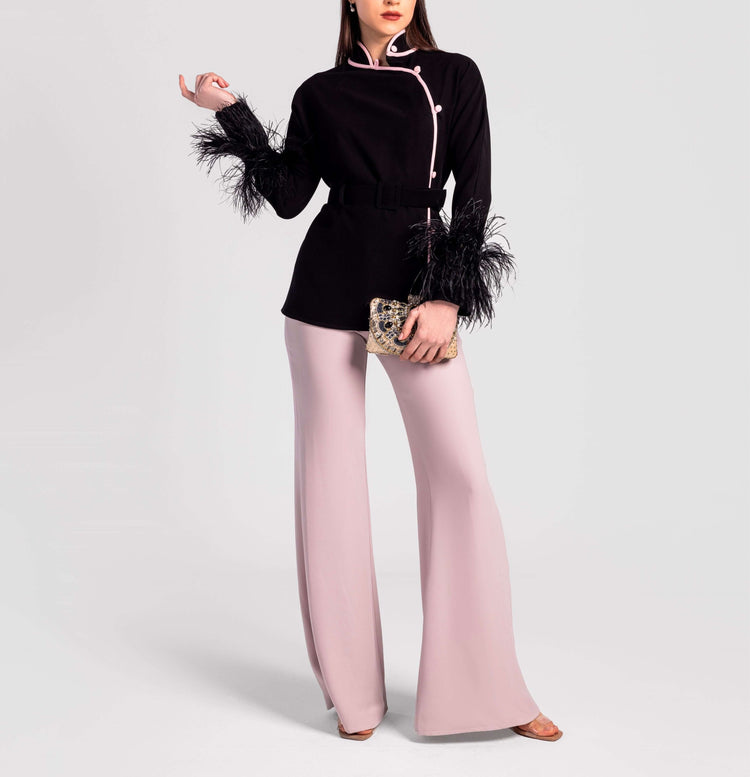 Woman modeling black belted top with feather cuffs and pale pink wide-leg pants, holding clutch