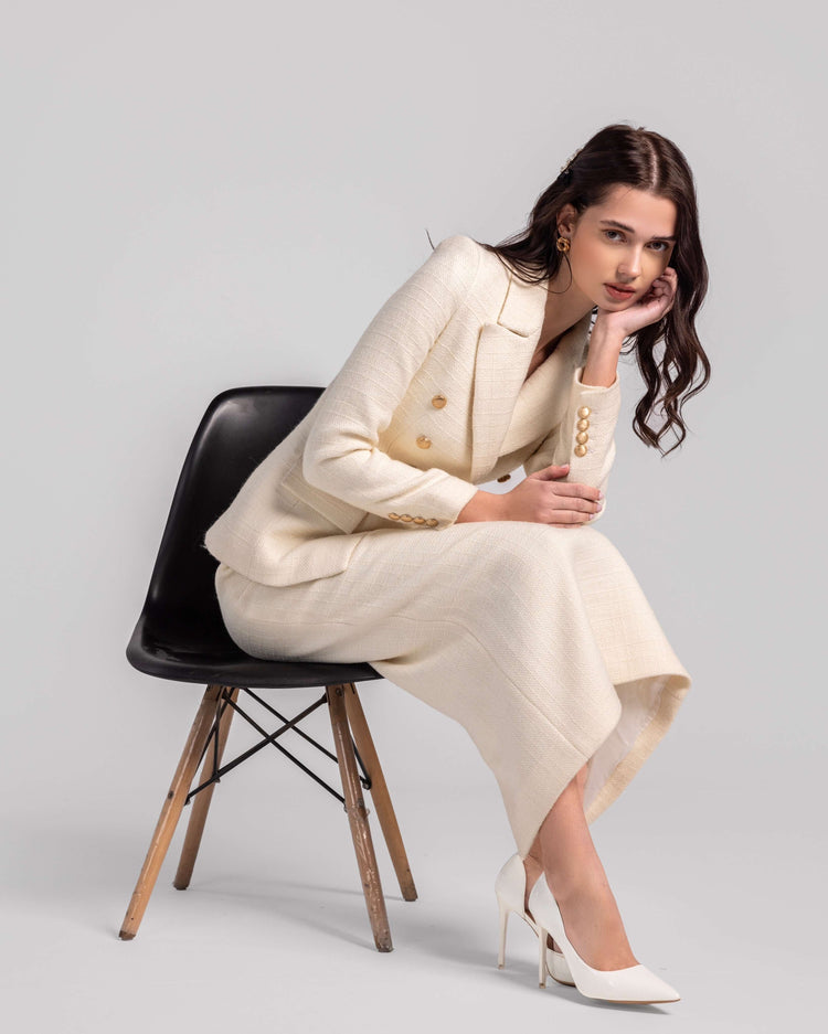 Woman in elegant cream suit and white heels sitting on black chair, minimalist studio
