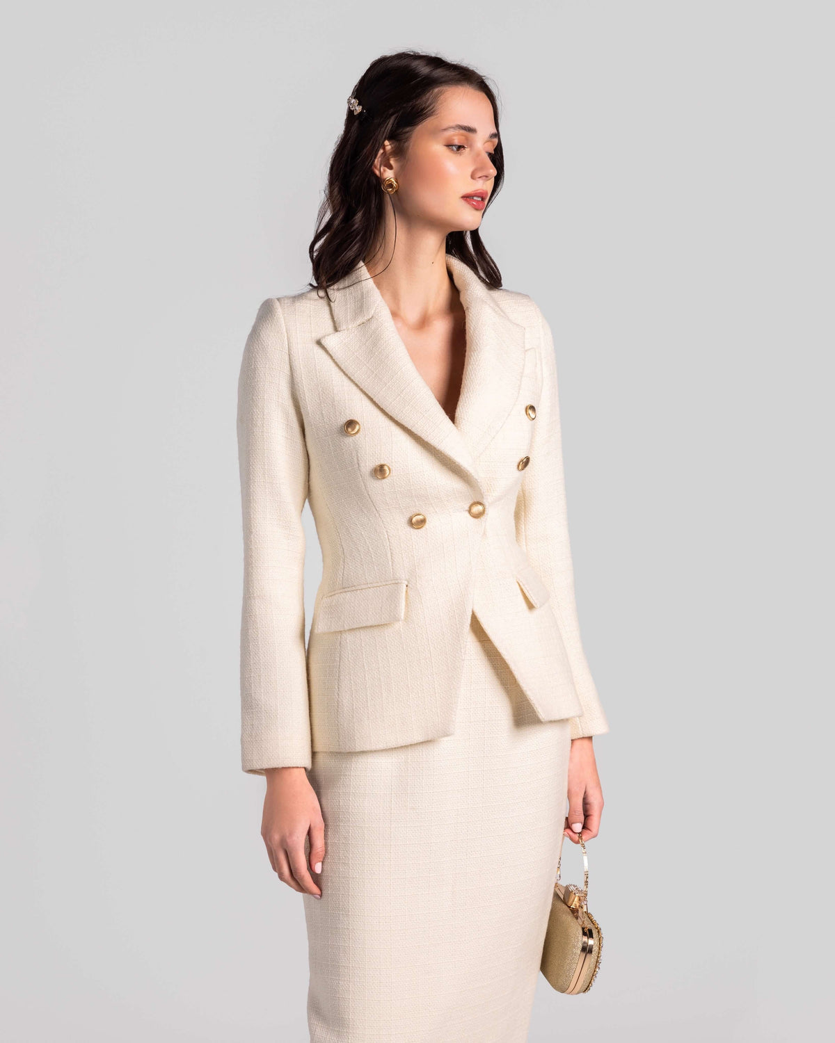 Woman in elegant cream double-breasted suit with gold buttons, holding a matching clutch