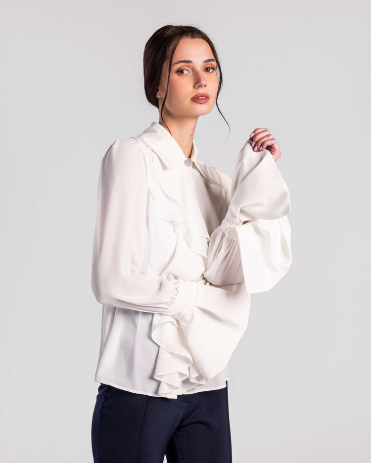 Woman in elegant white ruffled blouse with dramatic sleeves and dark tailored pants