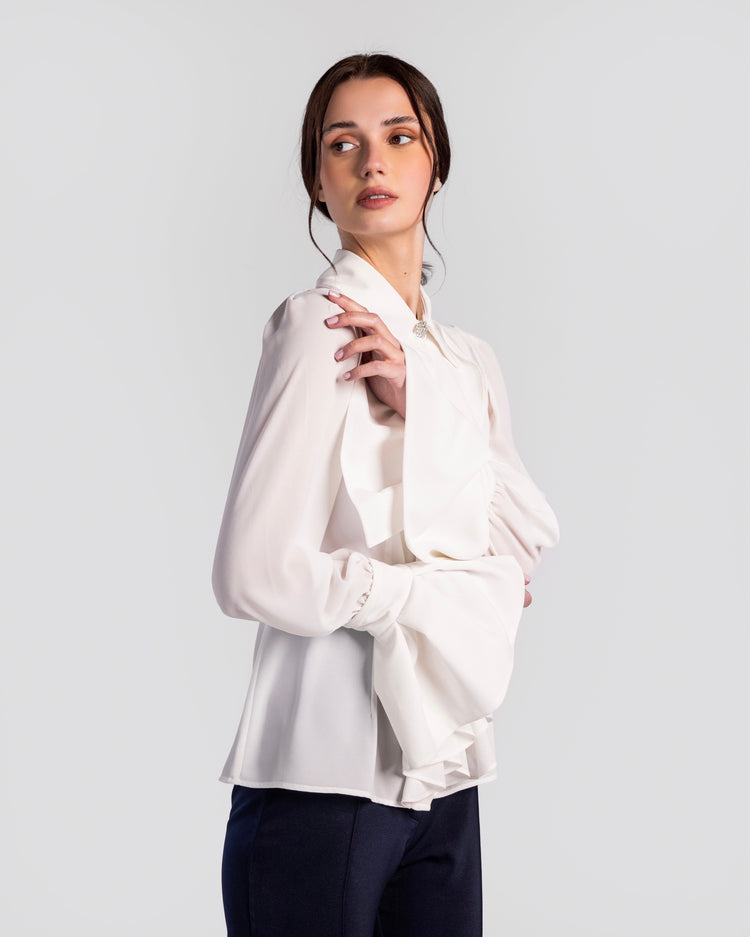 Woman wearing elegant white blouse with ruffled sleeves and black trousers on plain background