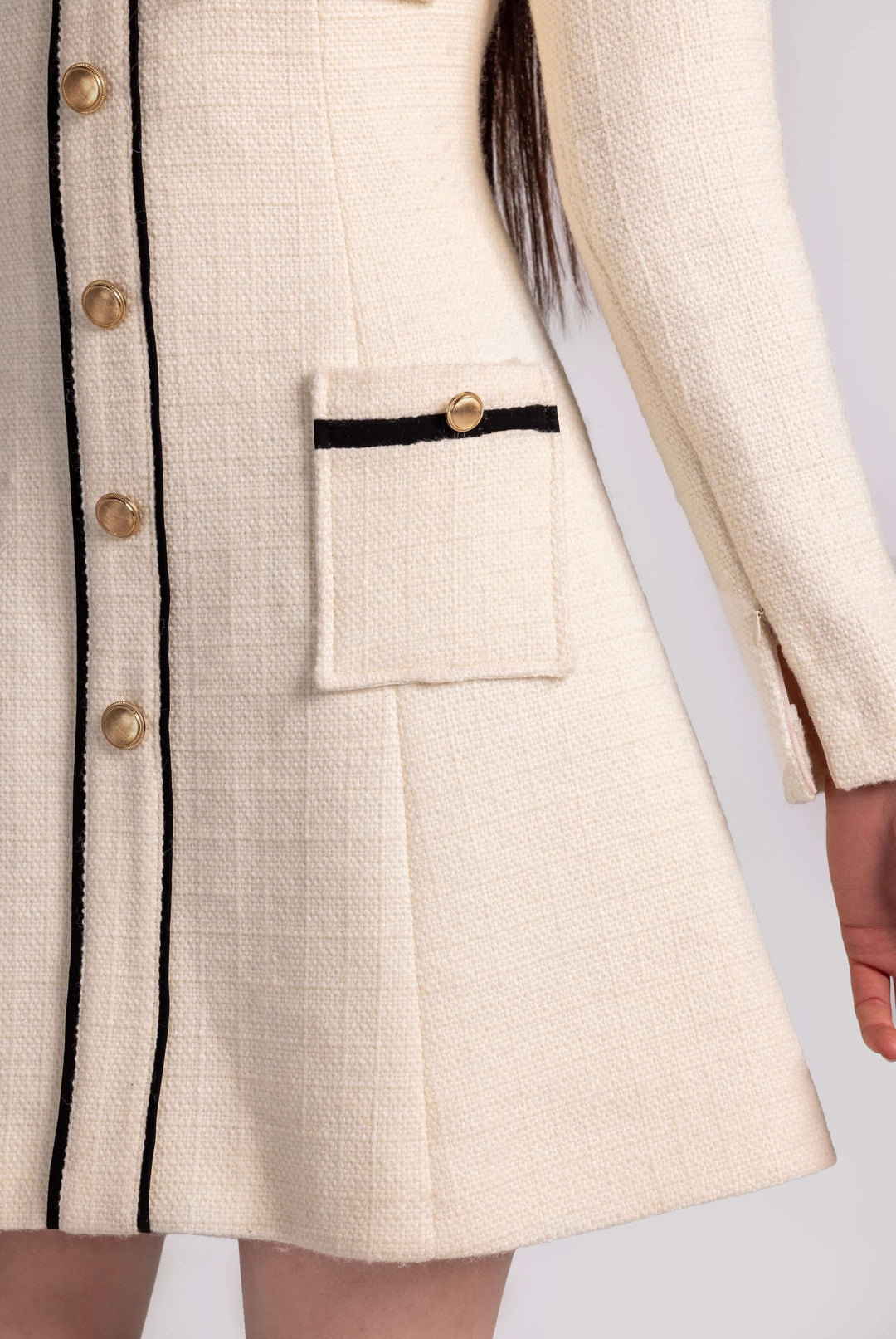 Close-up of cream tweed dress with gold buttons, black trim, and flap pocket detail