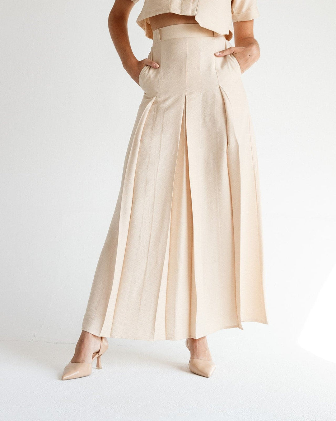 Woman wearing beige pleated high-waisted maxi skirt with matching heels and crop top