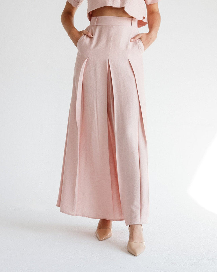 Woman wearing high-waisted blush pink wide-leg pleated pants with nude heels