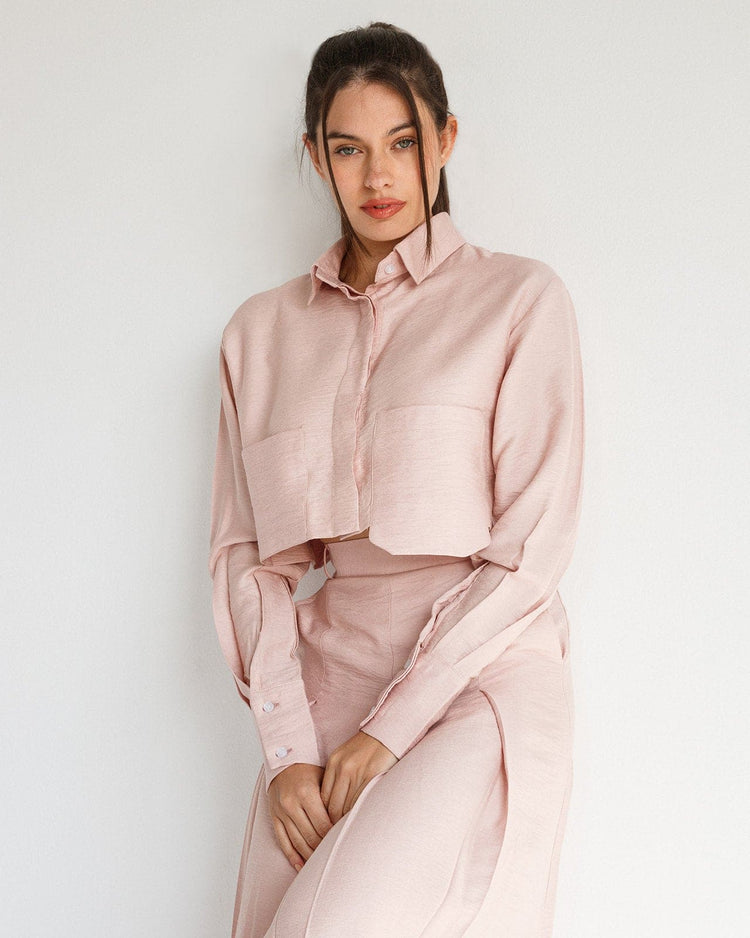 Woman wearing a light pink cropped shirt and matching high-waist skirt against a white wall