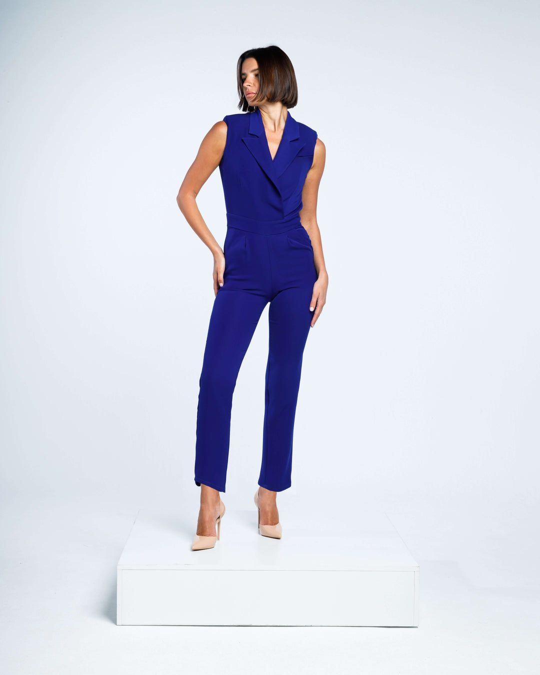 Woman wearing a sleeveless royal blue jumpsuit with tailored fit and beige heels