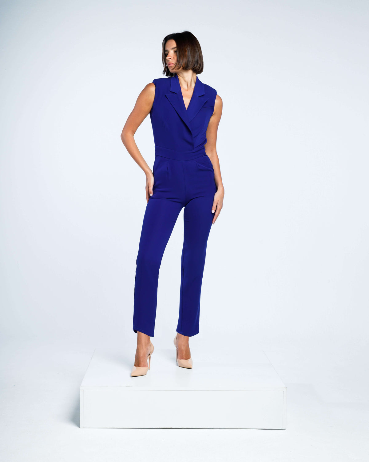 Woman wearing a sleeveless royal blue jumpsuit with tailored fit and beige heels