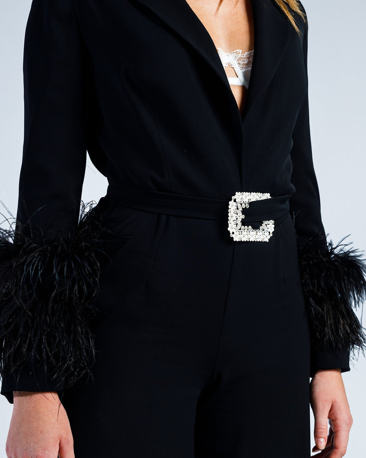 Black women's jumpsuit with feathered cuffs, white lace peek, and pearl belt buckle