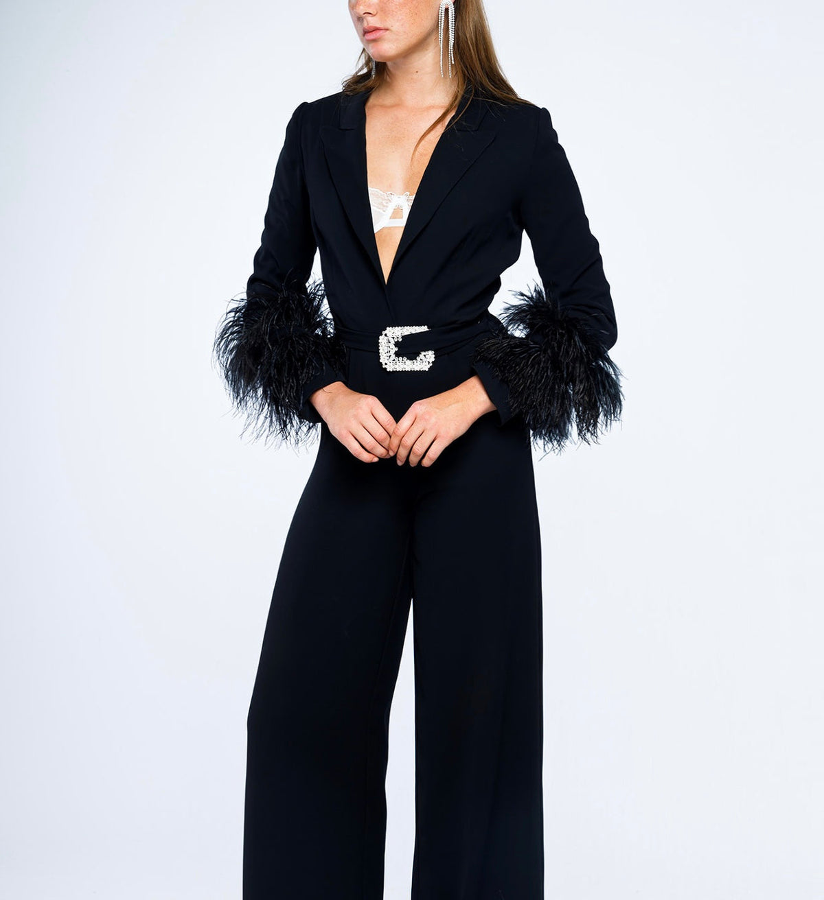 Woman modeling elegant black jumpsuit with feathered cuffs and crystal belt, fashion outfit