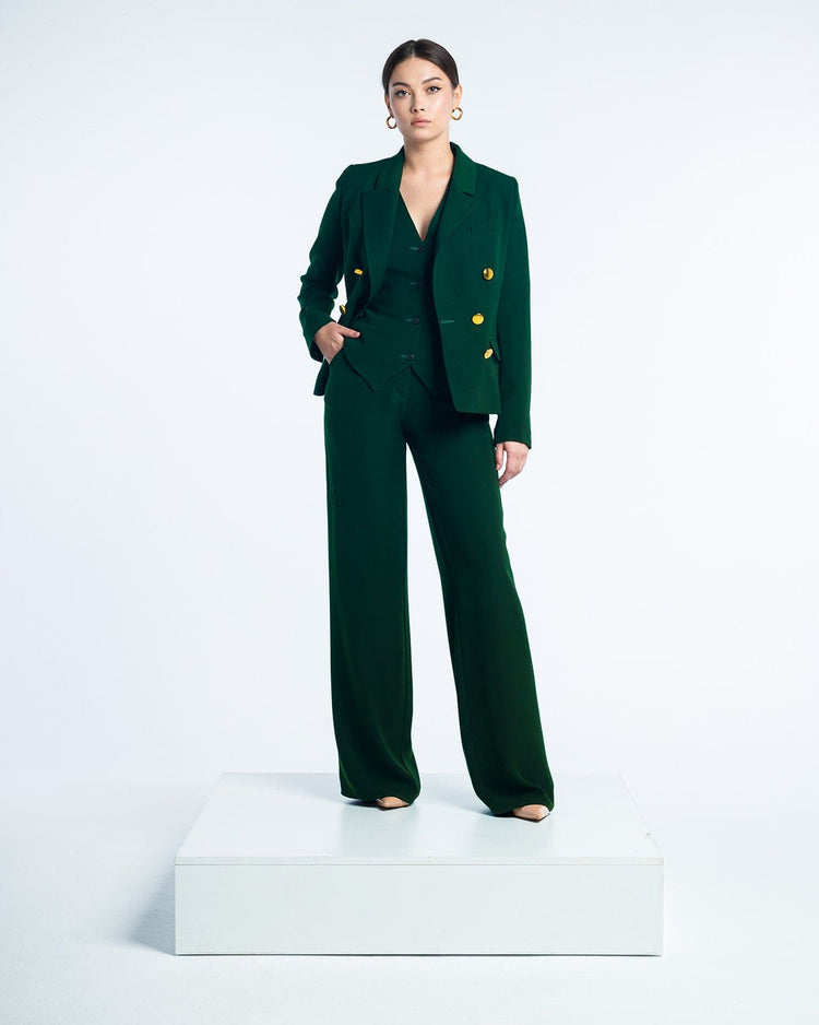 Woman in elegant dark green suit with gold buttons posing on a white platform studio