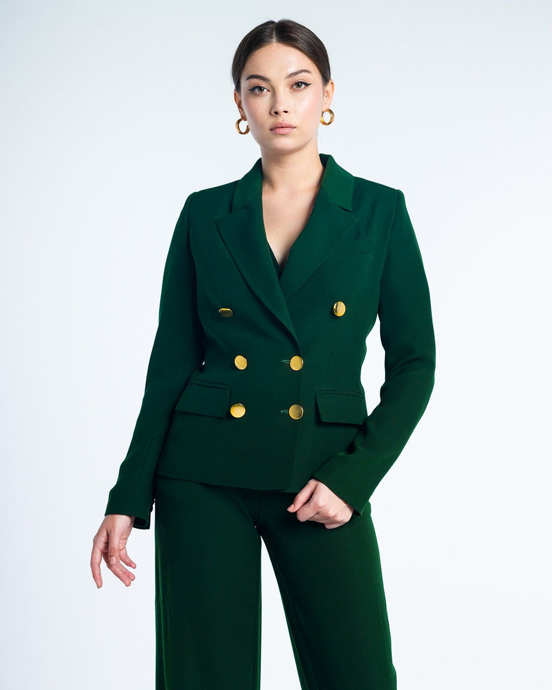Woman in emerald green double-breasted suit with gold buttons and hoop earrings