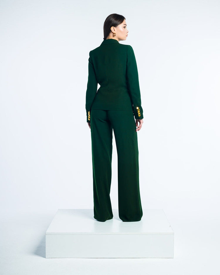 Woman in an elegant dark green pantsuit with gold button details, standing on a platform