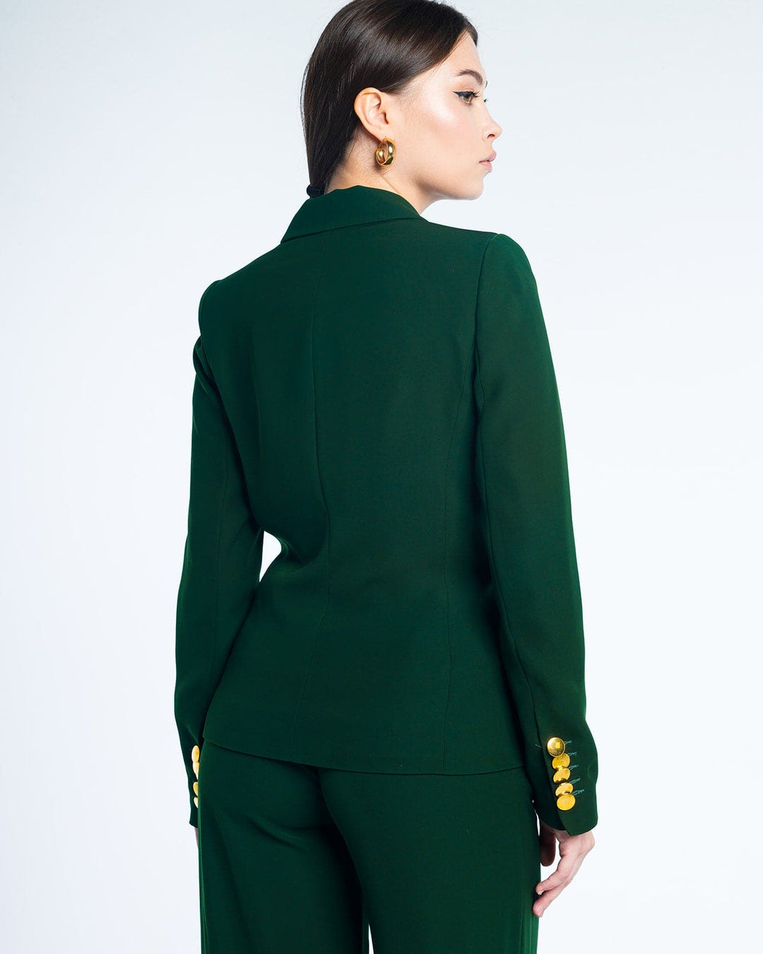 Woman in tailored dark green suit with gold button details, standing against a white background
