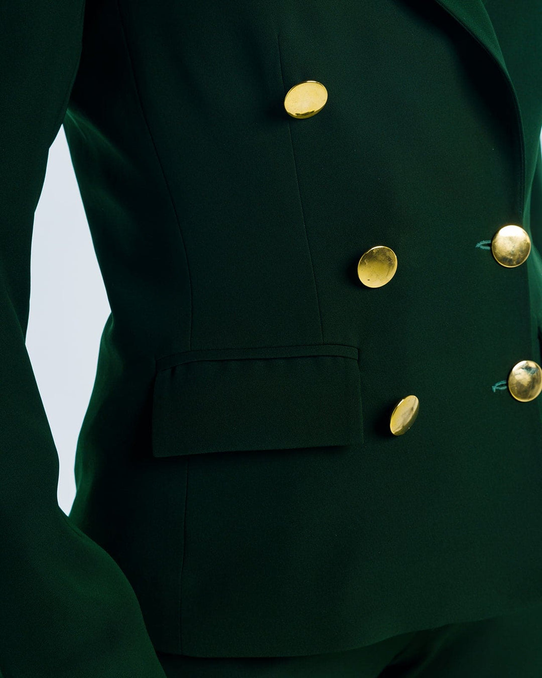 Close-up of tailored dark green blazer with gold buttons and a flap pocket