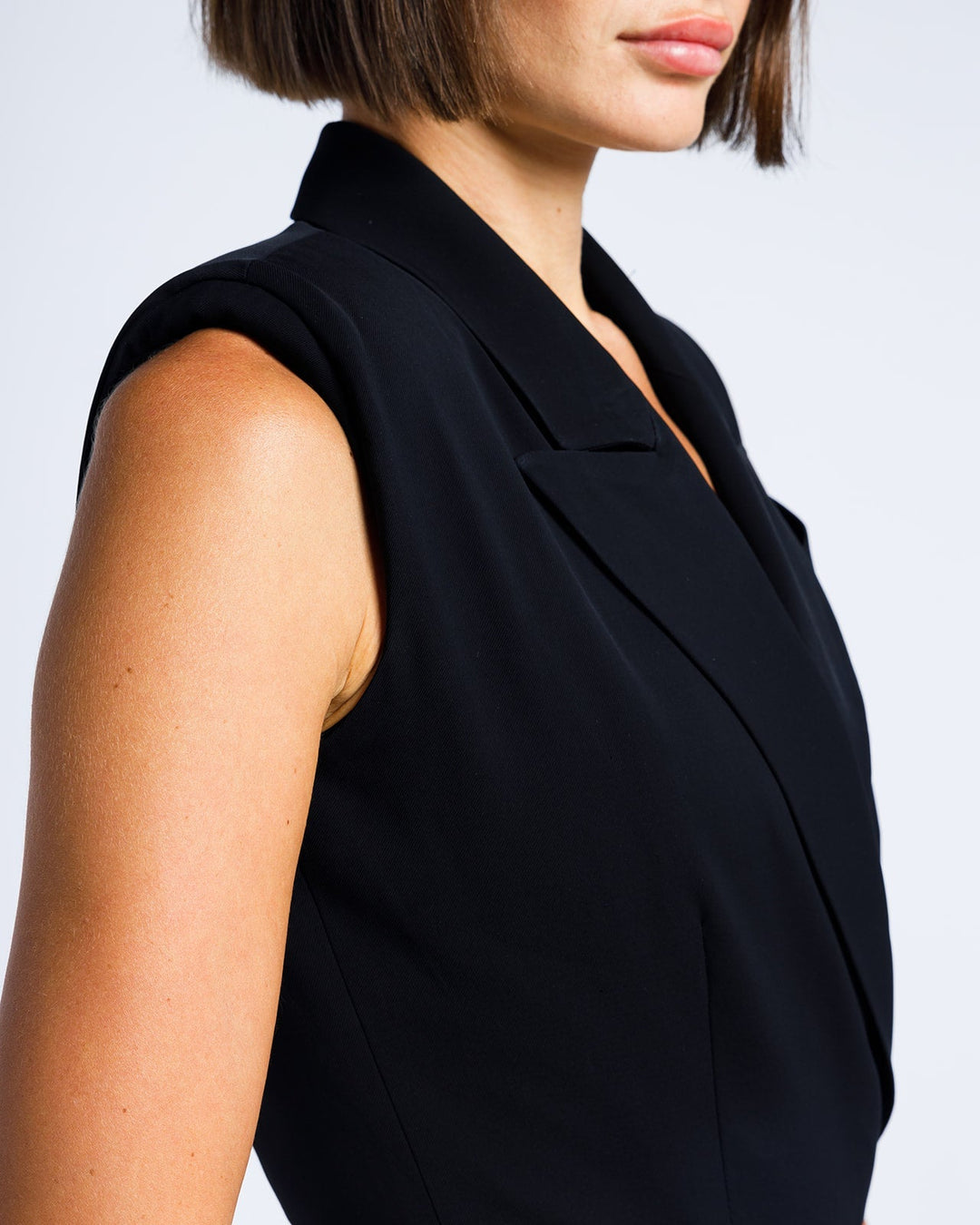 Woman wearing a sleeveless black tailored suit jacket with notched lapel