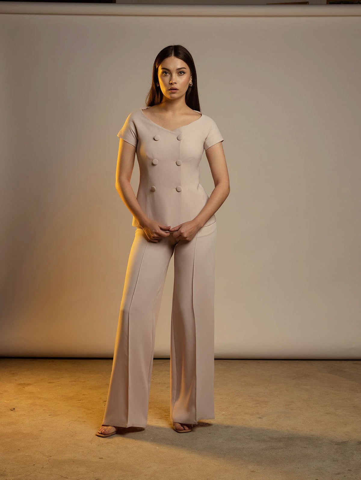 Woman modeling a beige short-sleeve wide-leg pantsuit with button details in studio