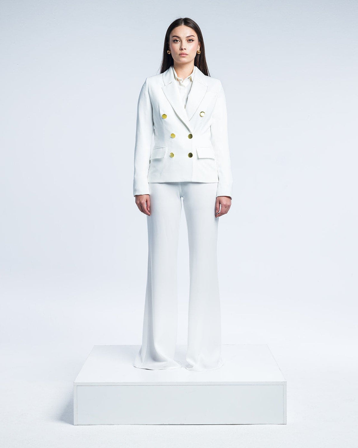 Woman in tailored white double-breasted suit with gold buttons, standing on platform