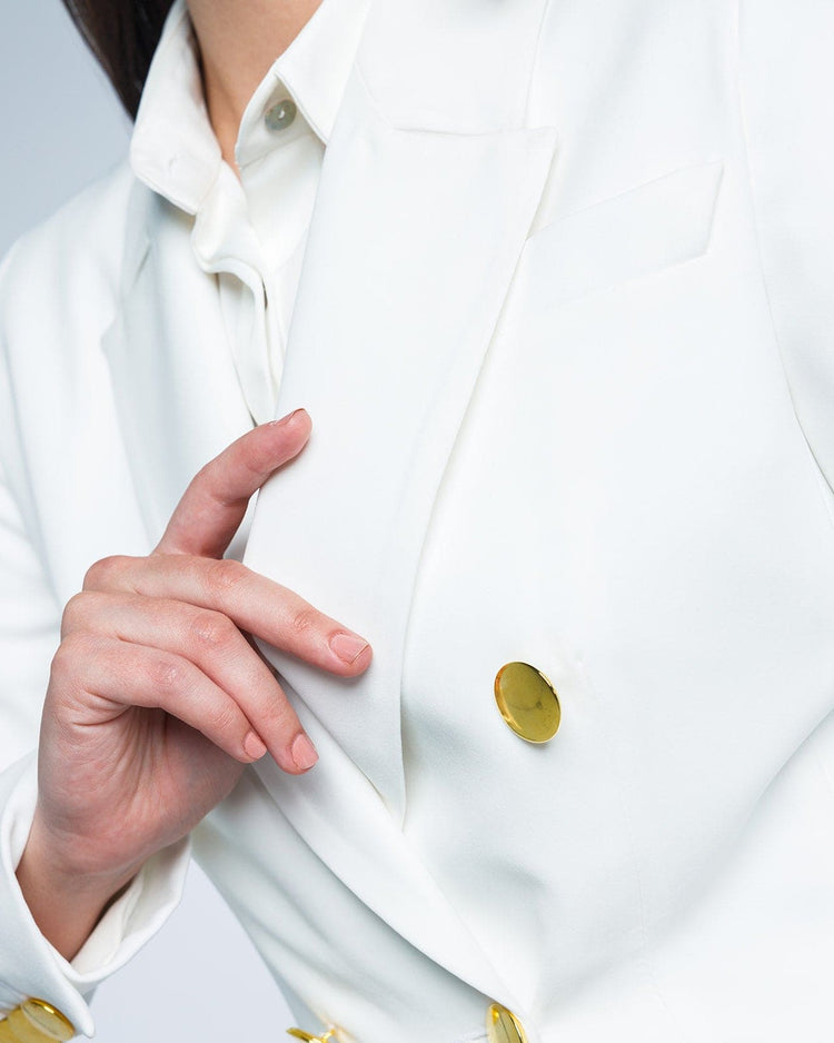 Close-up of a woman wearing a white tailored blazer with gold buttons and a collared shirt