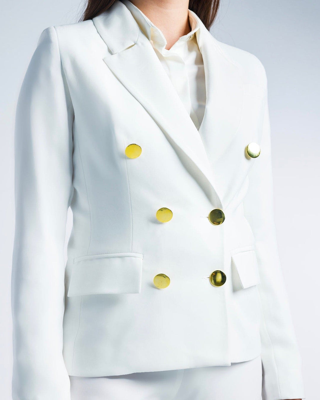 Woman wearing a tailored white double-breasted blazer with gold buttons