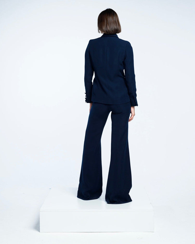 Woman in navy blue tailored suit with wide-leg pants, standing on white platform, back view
