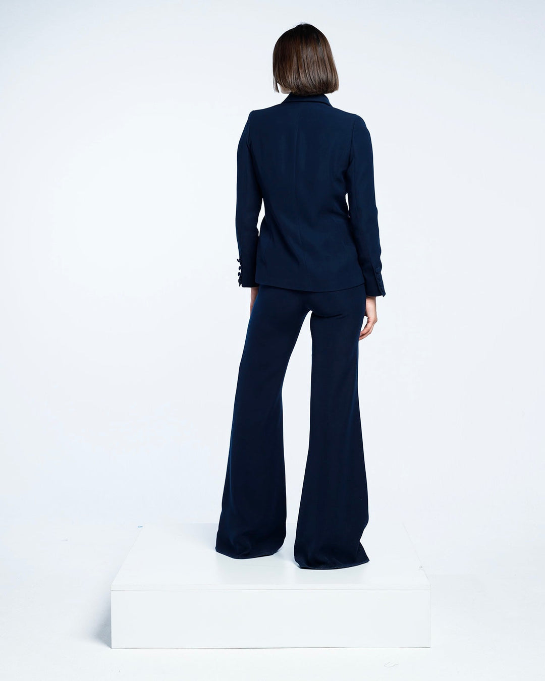 Woman in elegant navy blue pantsuit with flared trousers, standing on white platform