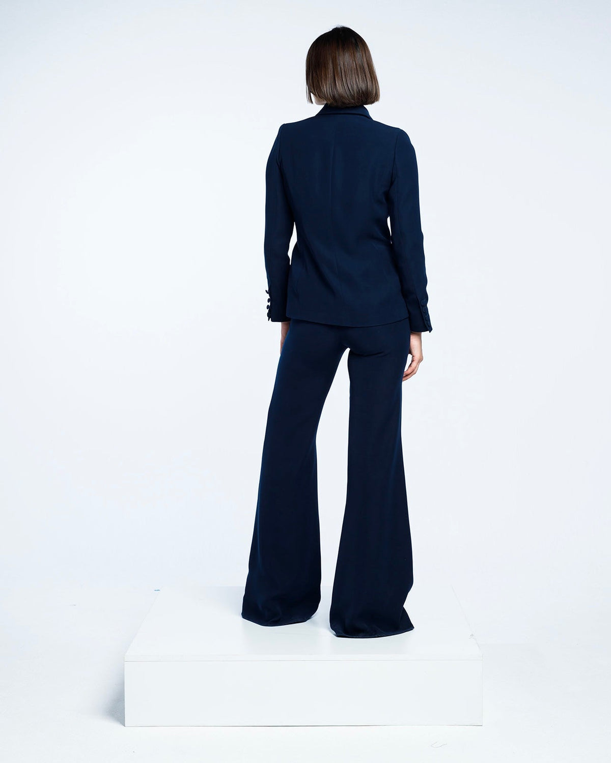 Woman in elegant navy blue pantsuit with flared trousers, standing on white platform