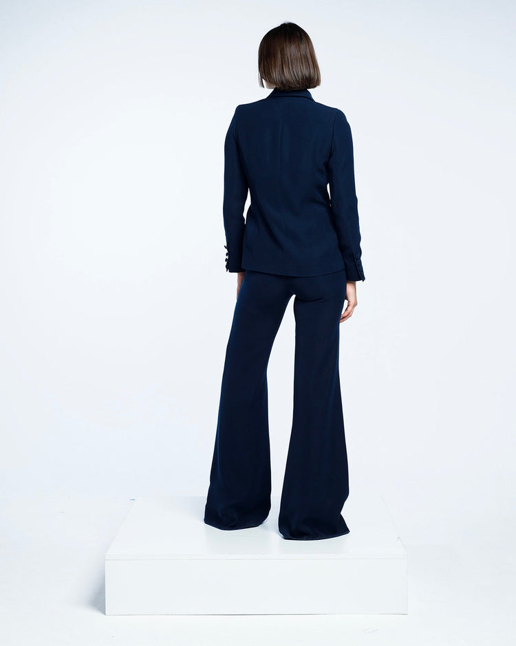 Woman in elegant navy blue pantsuit with flared trousers, standing on white platform