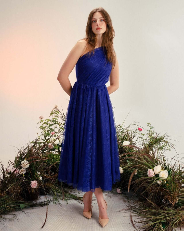 Woman in an elegant blue one-shoulder lace dress posing among flowers
