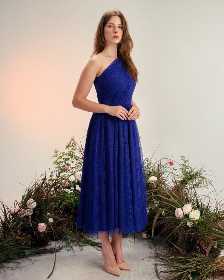Woman in elegant one-shoulder blue lace midi dress with nude heels, floral backdrop