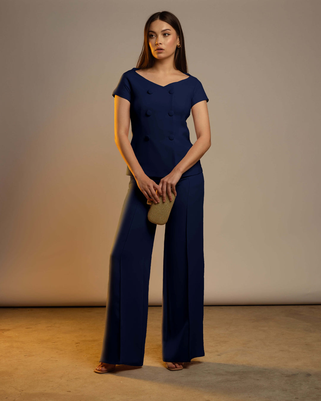 Woman in elegant navy blue pantsuit with wide-leg trousers, holding a gold clutch