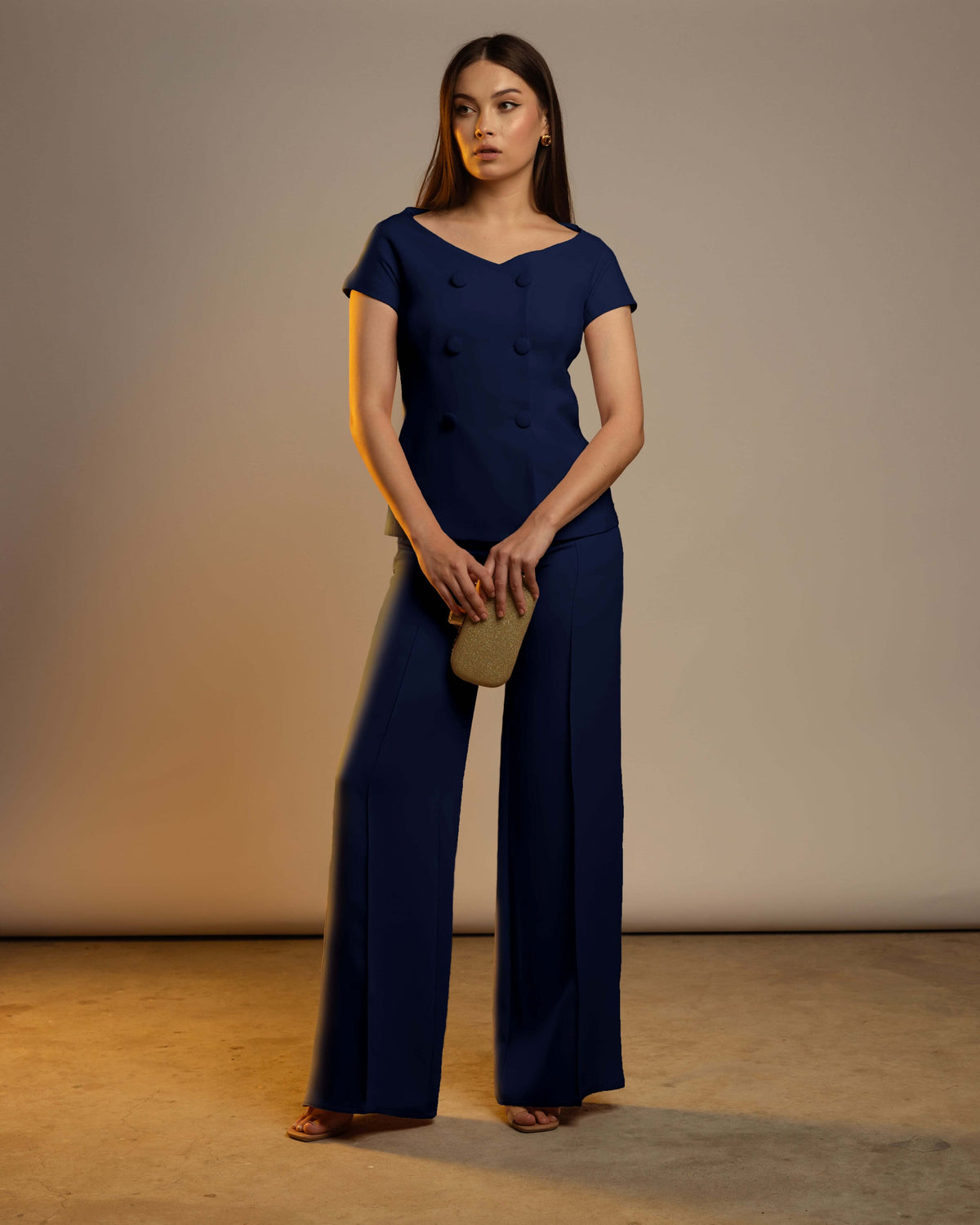 Woman in elegant navy blue pantsuit with wide-leg trousers, holding a gold clutch