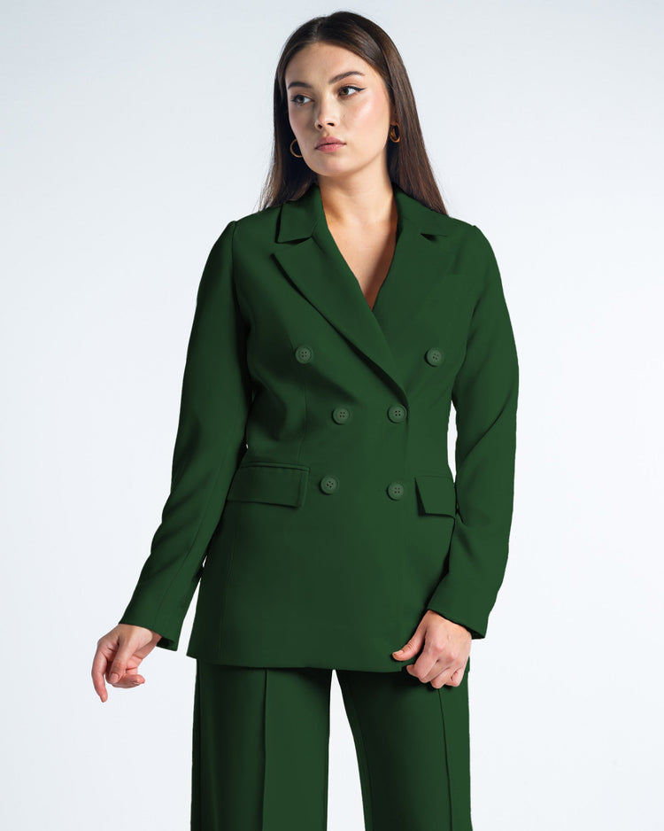Woman in elegant dark green double-breasted suit with gold hoop earrings, studio background.