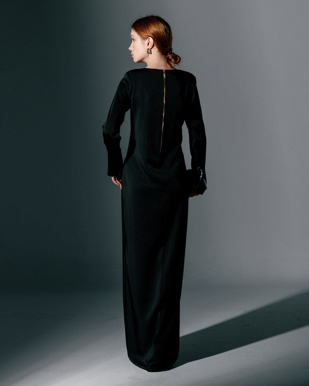 Woman wearing long sleeve black gown dress with back zipper, standing in studio setting