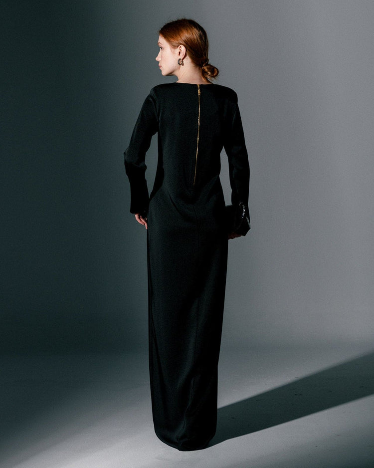 Woman wearing long sleeve black gown dress with back zipper, standing in studio setting