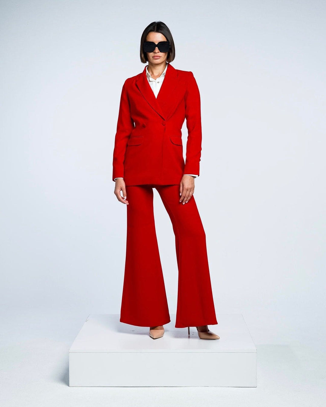 Woman in stylish red suit with flared pants, white shirt, nude heels, and black sunglasses