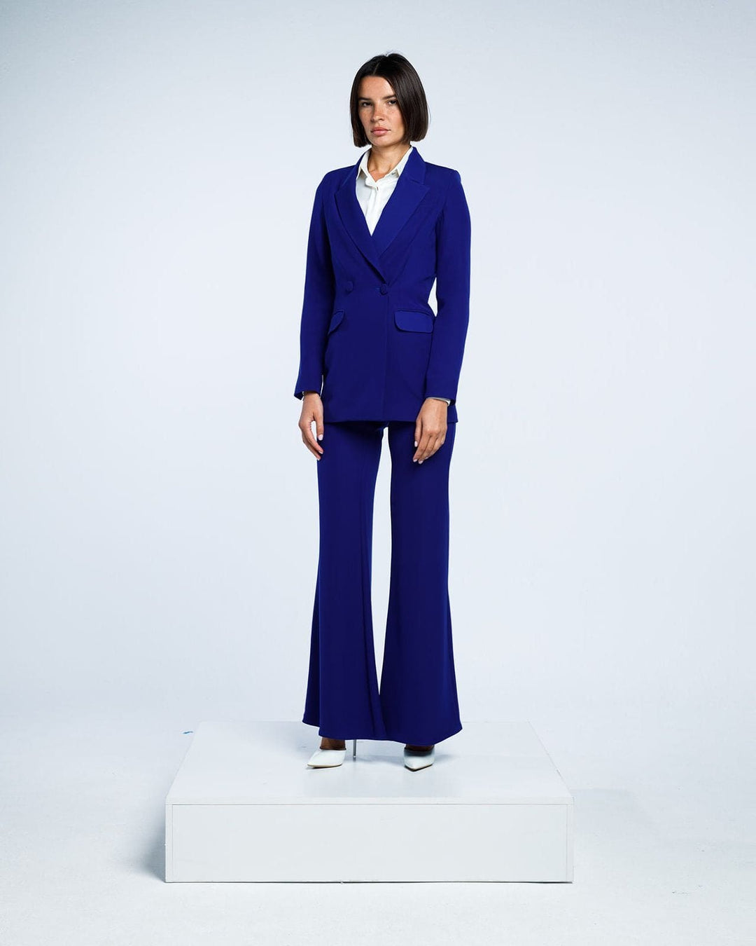 Woman in a royal blue tailored suit with flared pants and white blouse, studio background