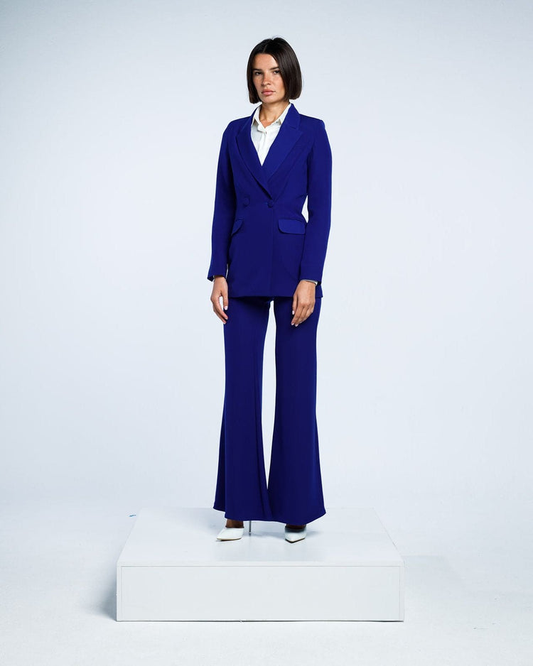Woman in a royal blue tailored suit with flared pants and white blouse, studio background