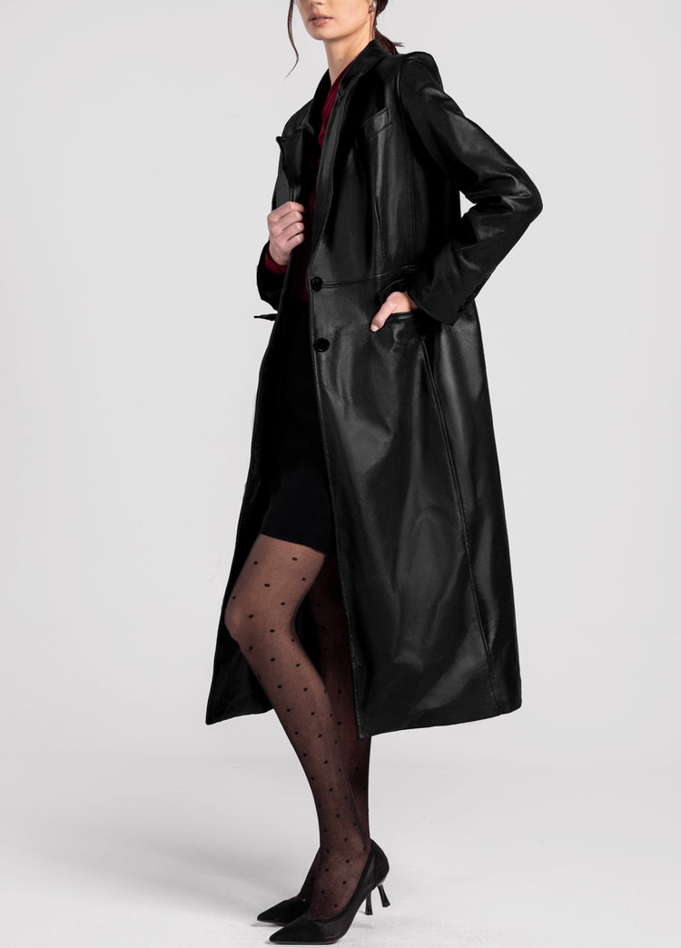 Woman wearing a long black leather trench coat, polka dot tights, and black heels