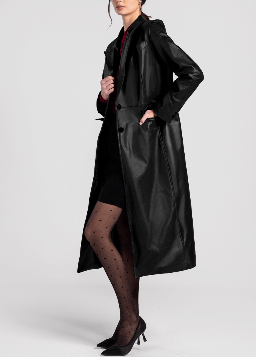 Woman wearing a long black leather trench coat, polka dot tights, and black heels