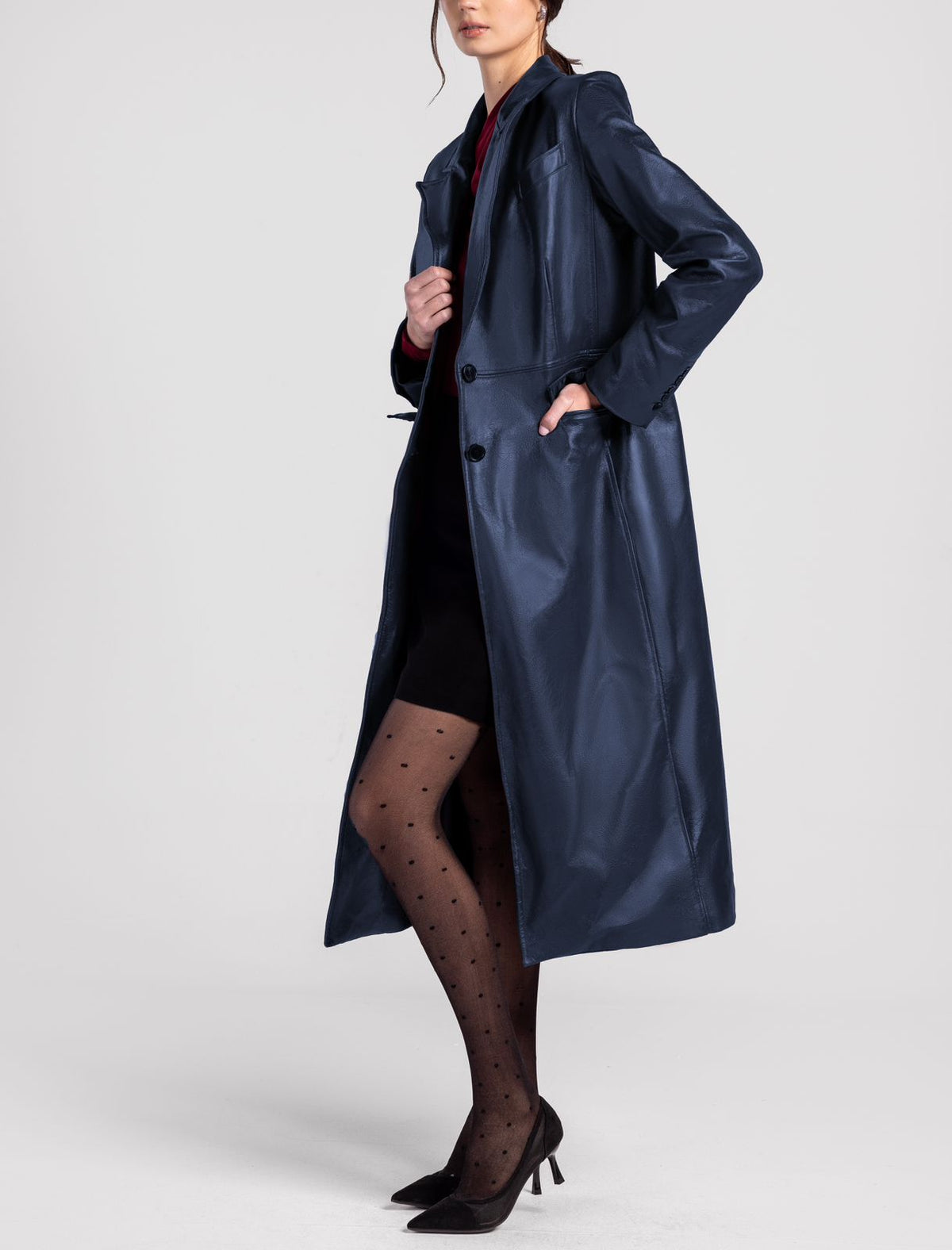 Woman wearing a long blue leather trench coat, black dotted tights, and pointed heels