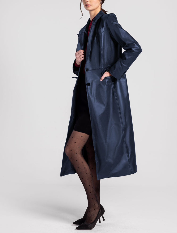 Woman wearing a long blue leather trench coat, black dotted tights, and pointed heels