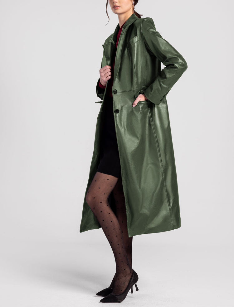 Woman wearing long green faux leather trench coat, black polka dot tights, and heels